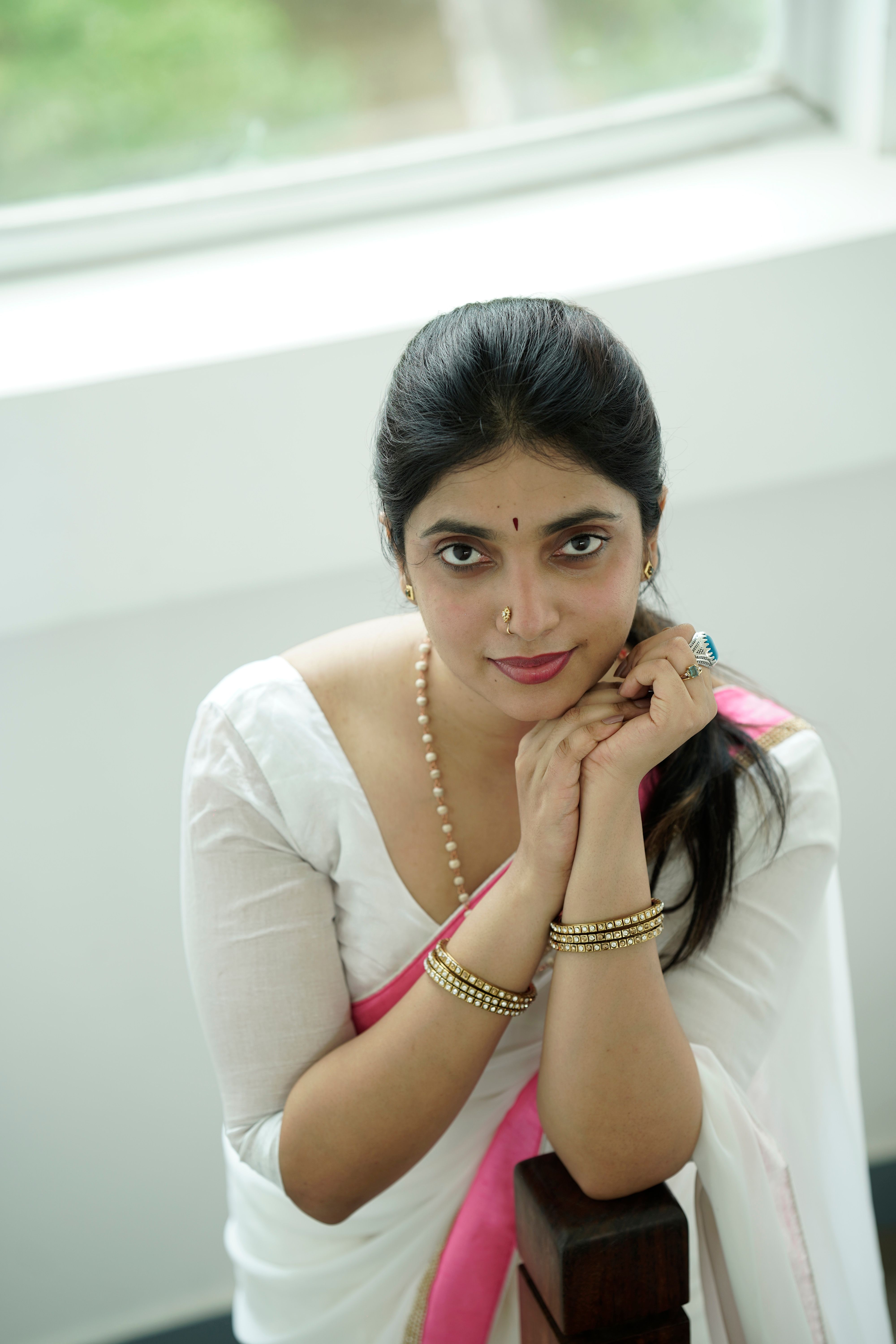 Portrait of a South Asian woman in a white saree with pink accents, adorned with traditional jewelry, exuding elegance.