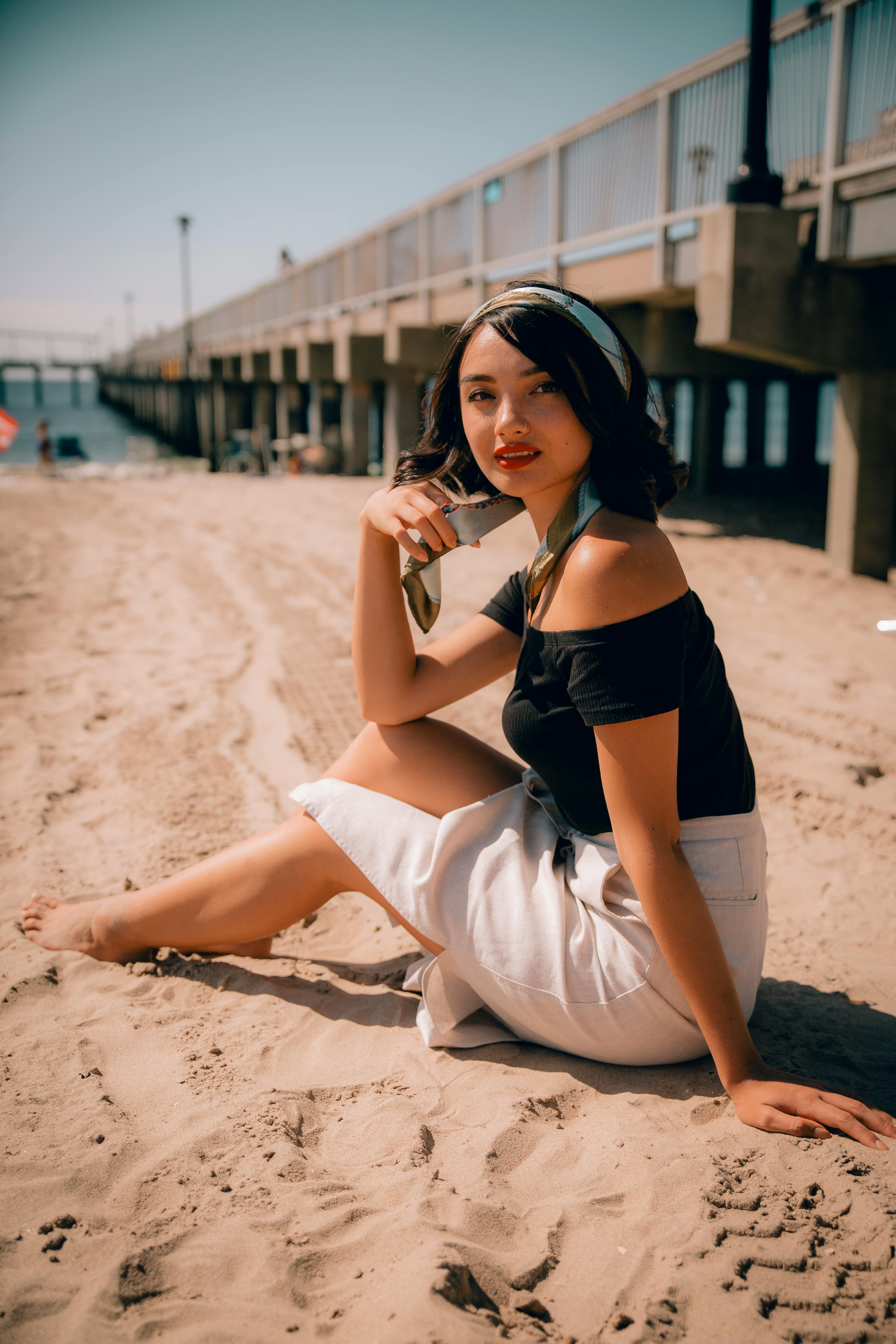 一位身着夏装的别致女子坐在码头边的沙滩上，散发着优雅的气息