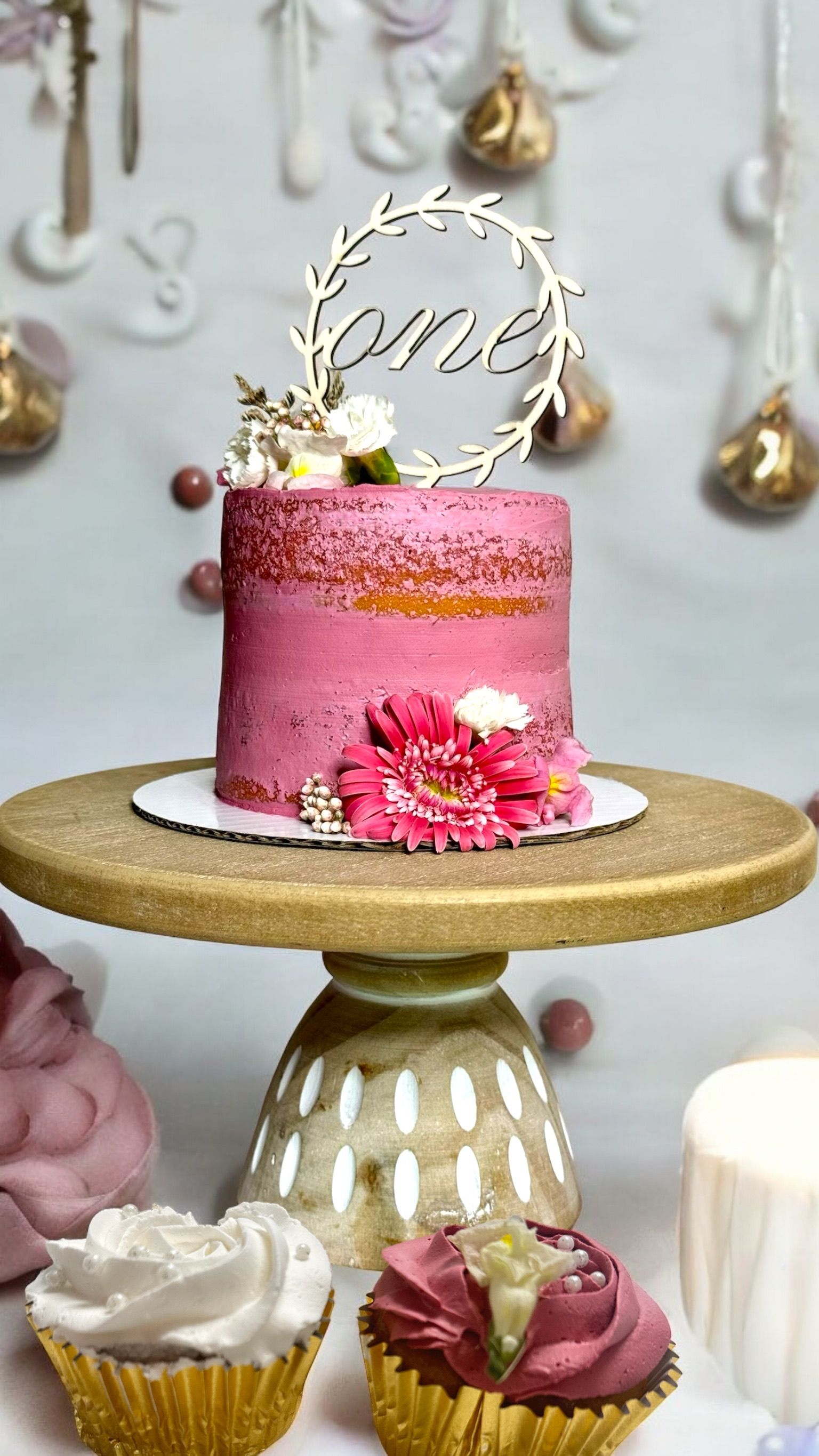 Pink cake and cupcakes with floral decor for a first birthday celebration.