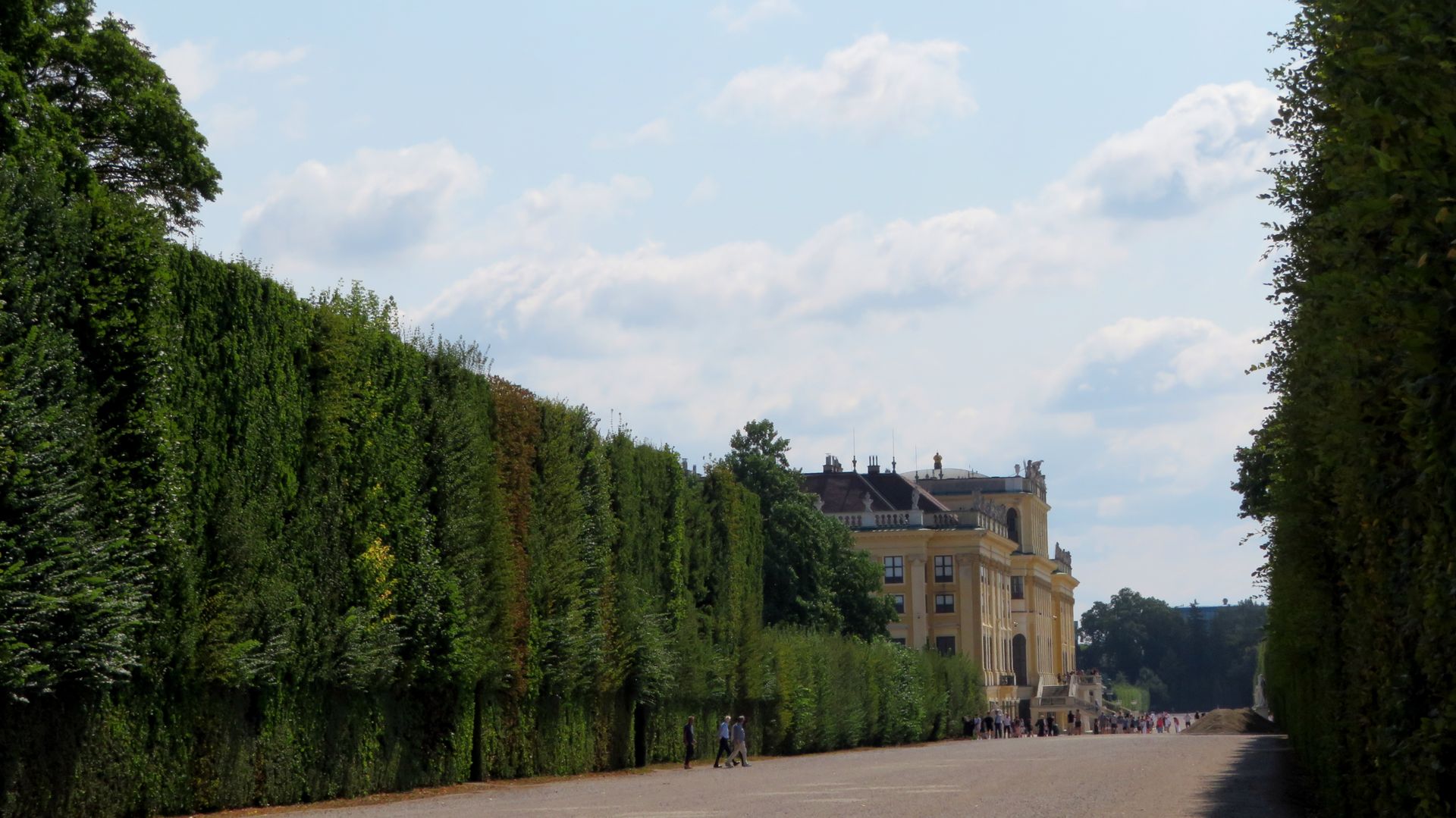 Elegant palace with manicured hedges and trees on a sunny day.