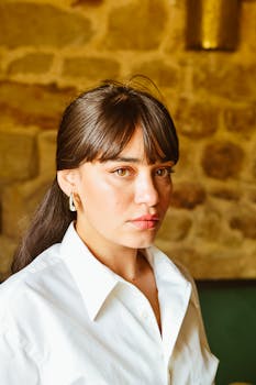 Portrait of a woman in a white shirt against a stone wall background.