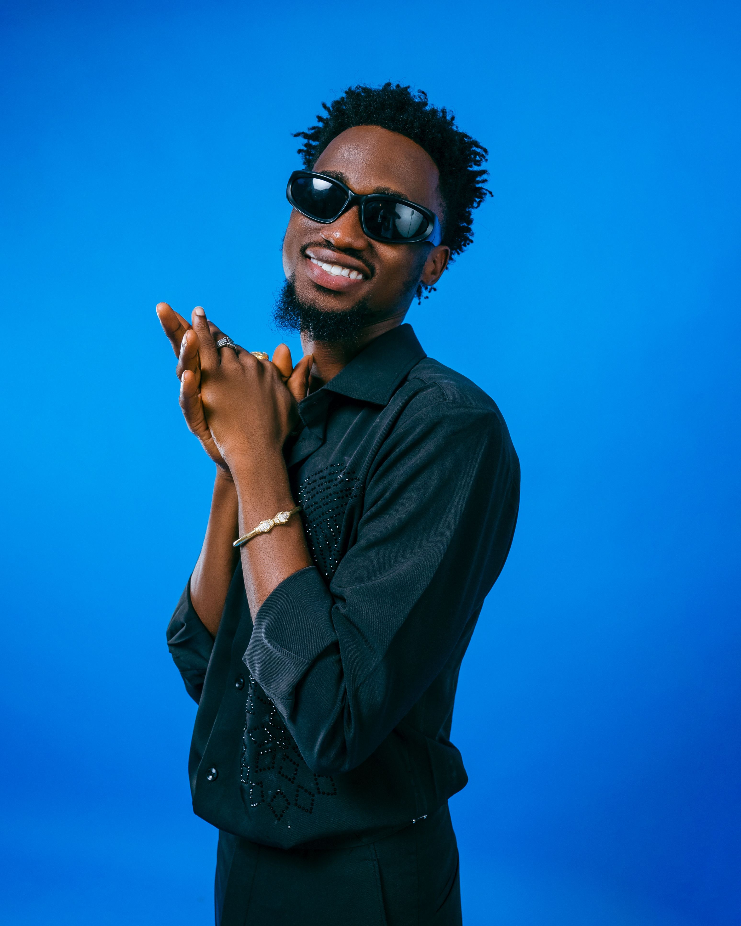 Fashionable man in black attire with sunglasses on blue background.