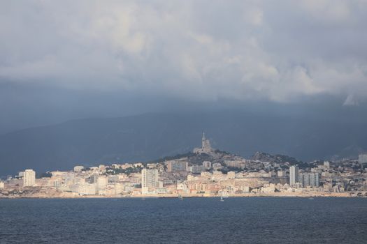 Panoramic view of Marseille skyline with Notre-Dame de la Garde under cloudy skies.