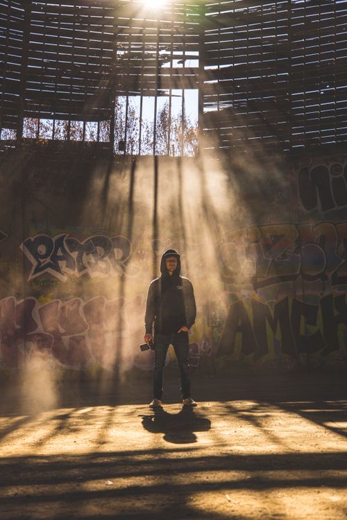 Free Silhouetted figure in hoodie amidst sunbeams and urban graffiti setting. Stock Photo