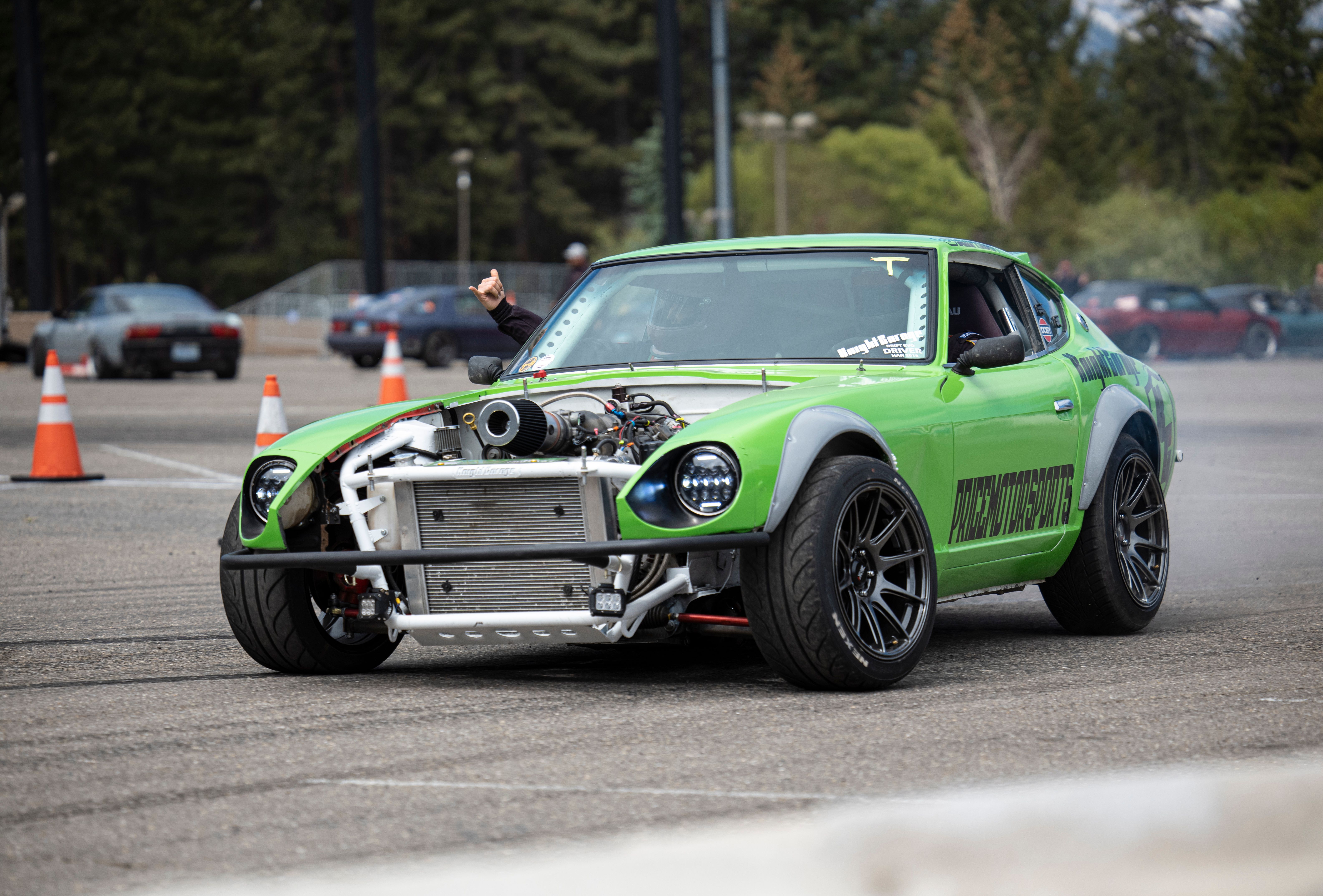 A vibrant green sports car drifts on a track with orange cones, showcasing driving skills outdoors.