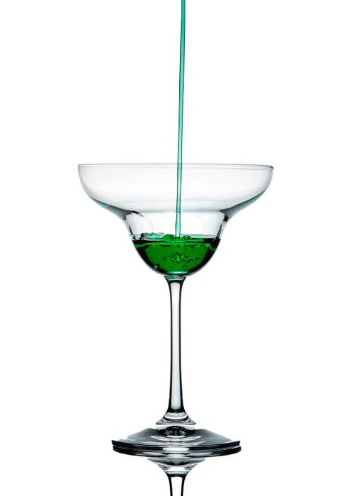Free Refreshing green liquid being poured into a clear cocktail glass isolated on white. Stock Photo