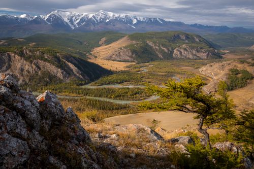 Free Breathtaking view of a vast mountain valley with a winding river and snowcapped peaks under a partly cloudy sky. Stock Photo