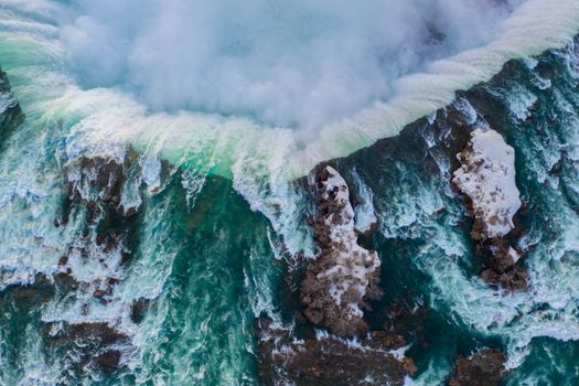 Stunning aerial shot of Niagara Falls cascading over rock formations with mist rising.