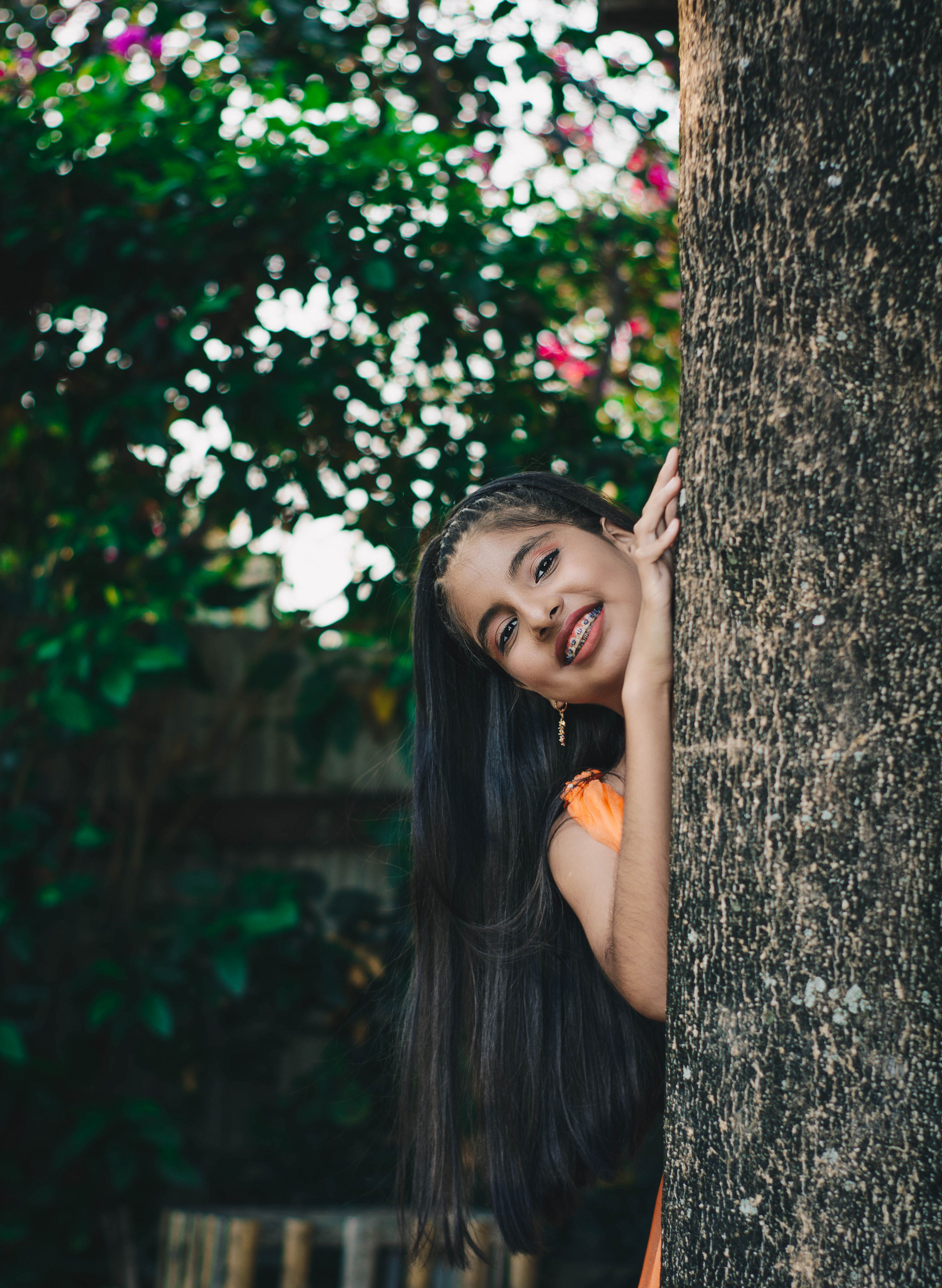 Smiling Girl Peeking from Behind a Tree Outdoors · Free Stock Photo