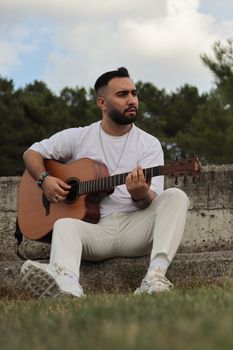 A man in white attire plays an acoustic guitar outdoors, evoking a serene musical vibe.