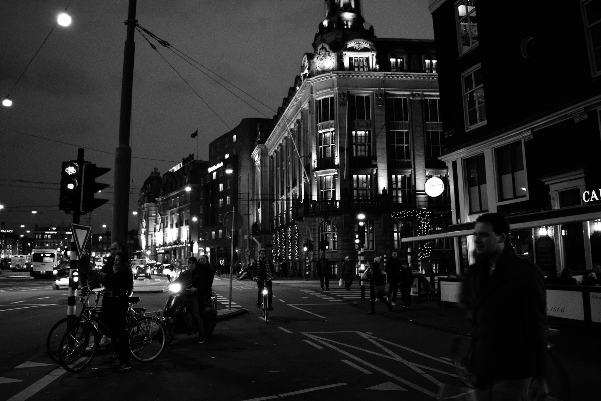 Black and white nighttime street scene in central Amsterdam showcasing bikes, traffic, and historic architecture.