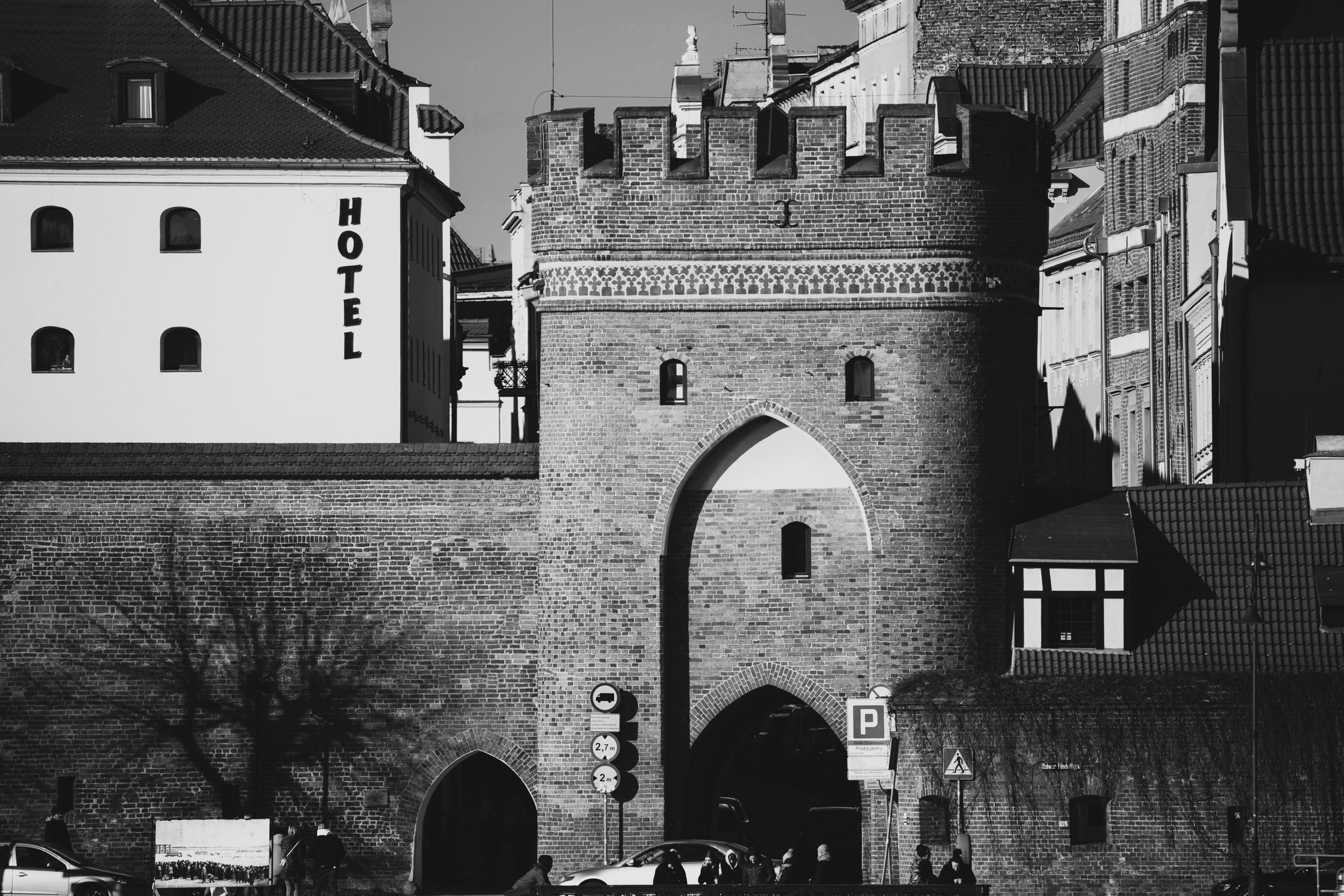 Black and white photo of a historic brick gateway with adjacent buildings and a hotel sign.