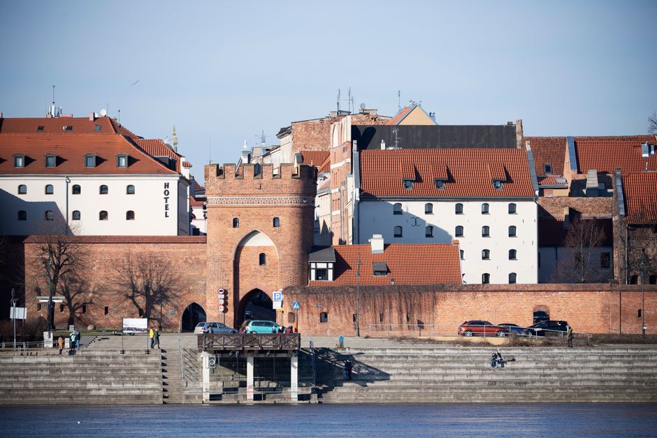 Toruń's medieval city gate by the riverside, showcasing red-brick architecture and urban charm.