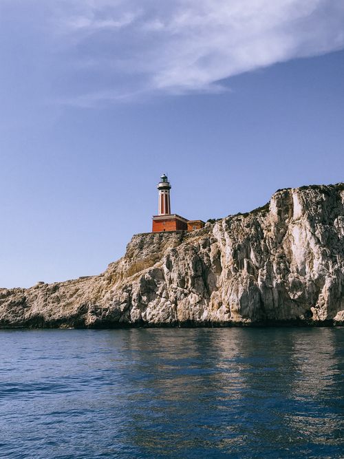 Free Scenic view of Punta Carena Lighthouse on a rocky cliff in Capri, Italy under a clear blue sky. Stock Photo