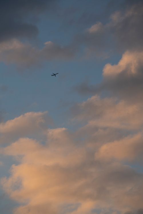 Free Silhouette of an airplane flying against a dramatic cloudy sunset sky. Stock Photo