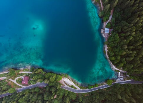 从令人惊叹的鸟瞰视角看去，一个宁静的森林湖被郁郁葱葱的绿色植物和蜿蜒的道路环绕着