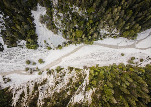 Drone shot capturing a winding riverbed through lush green forests and rocky terrains.