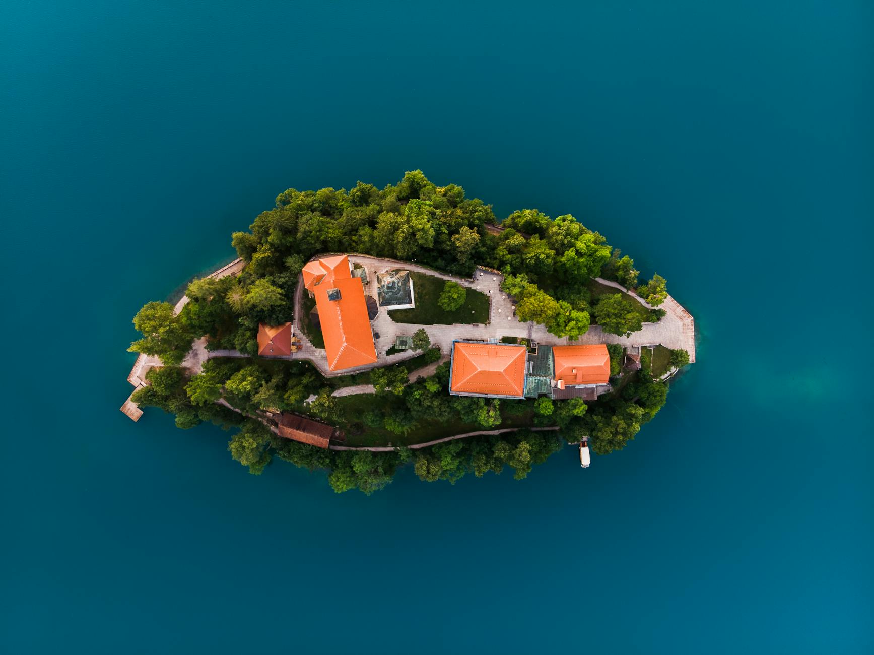 Discover a picturesque island surrounded by blue waters, captured from above, showcasing lush greenery and serene architecture.