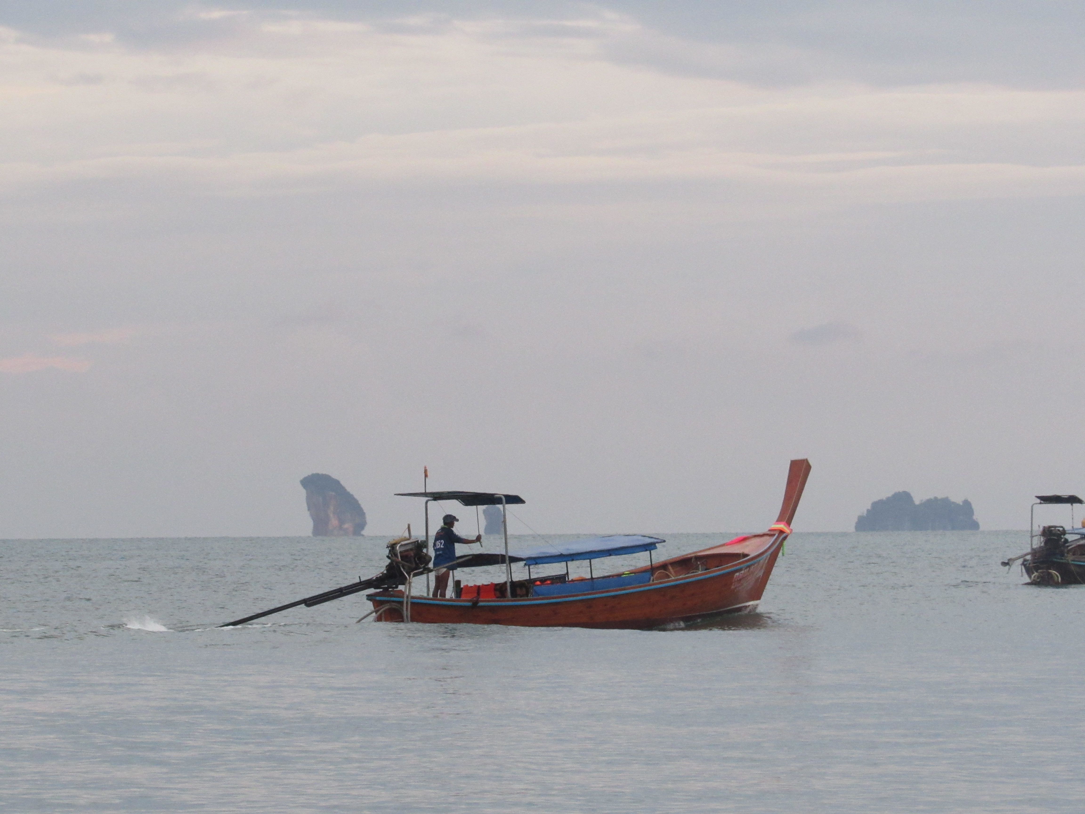 Scenic view of a traditional Thai longtail boat on a calm ocean with distant islands. Scenic view of a traditional Thai longtail boat on a calm ocean with distant islands.