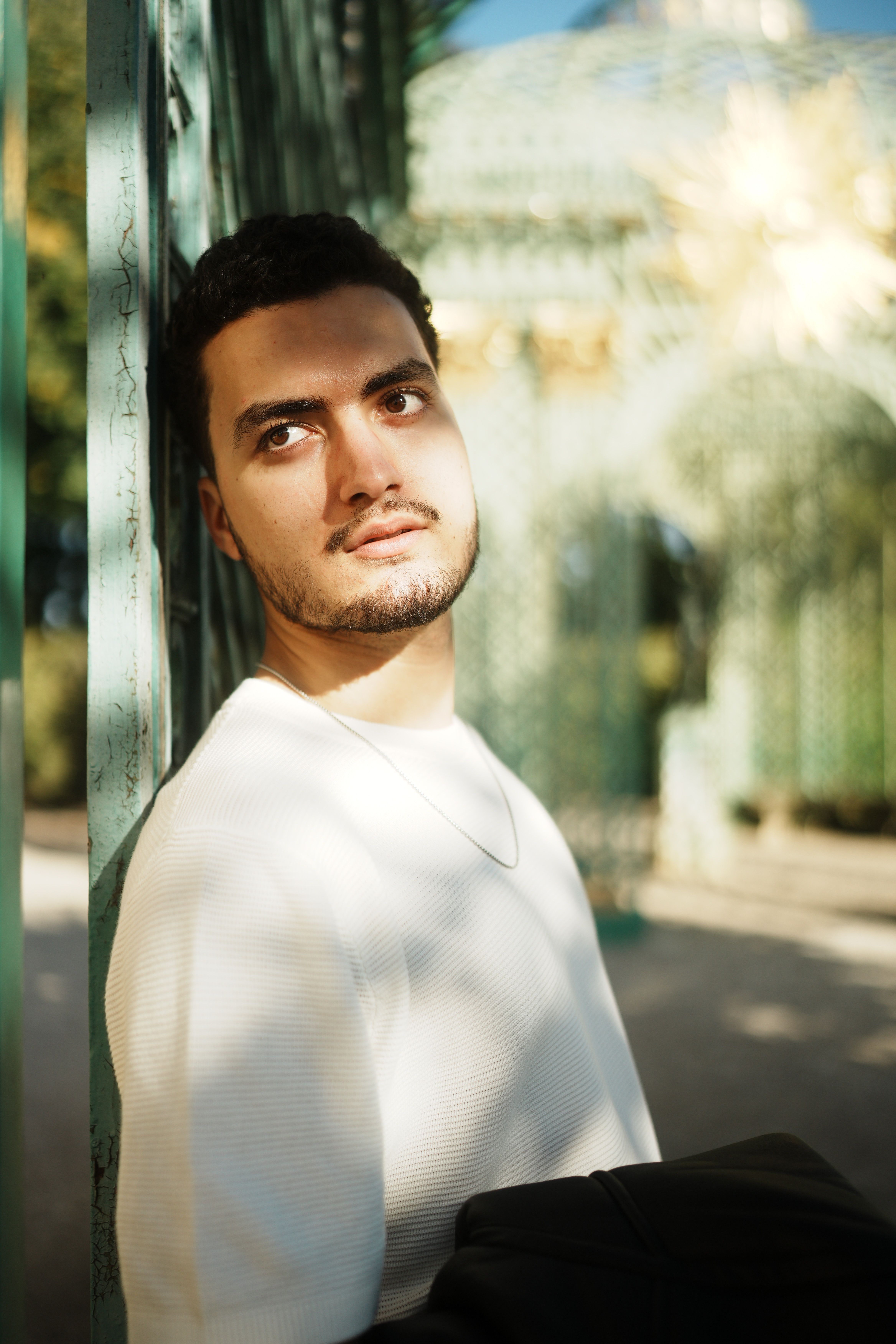 Young man in thoughtful pose against an ornate metal structure outdoors.