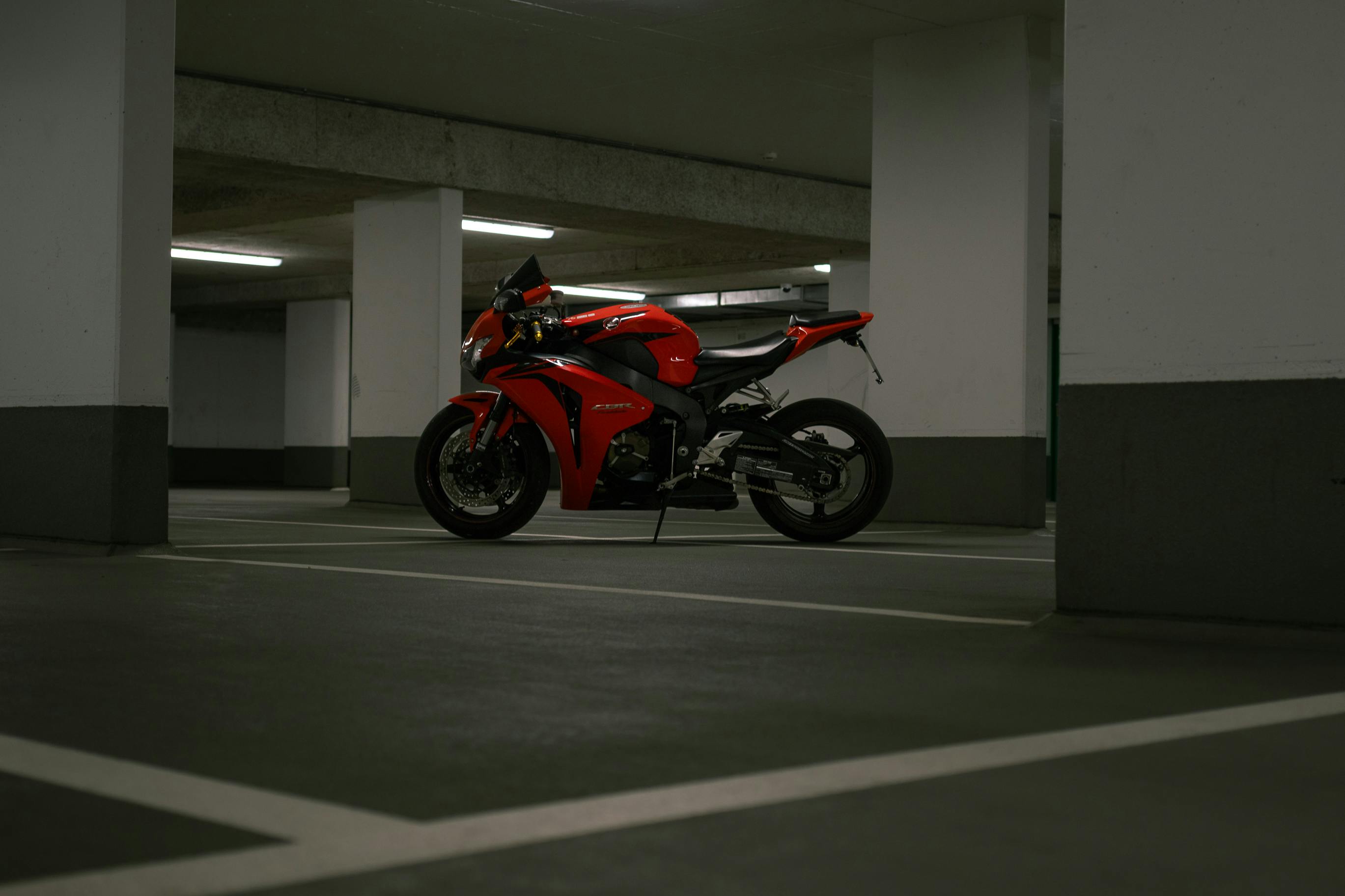 A sleek red sports motorcycle is parked in a dimly lit urban parking garage.