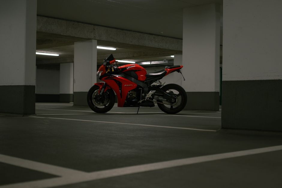 A sleek red sports motorcycle is parked in a dimly lit urban parking garage.