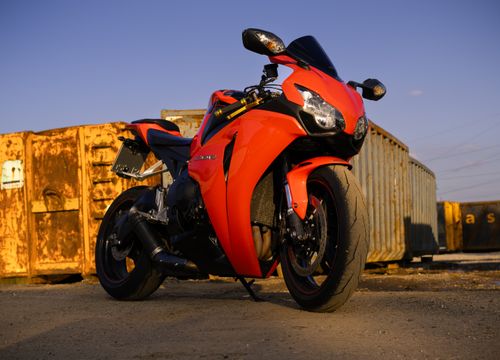 Free A sleek red motorcycle photographed against an urban industrial backdrop at sunset. Stock Photo