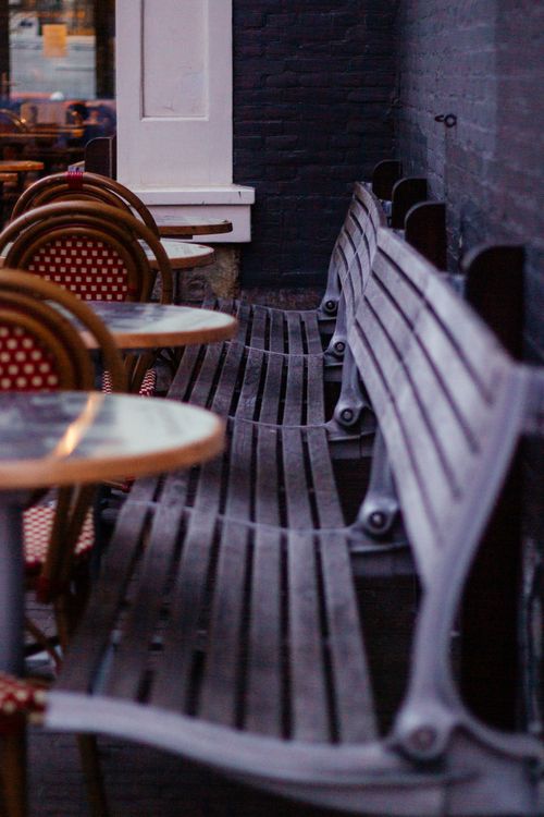 Free Cozy outdoor cafe terrace in Amsterdam featuring wooden benches and wicker chairs, captured in soft evening light. Stock Photo