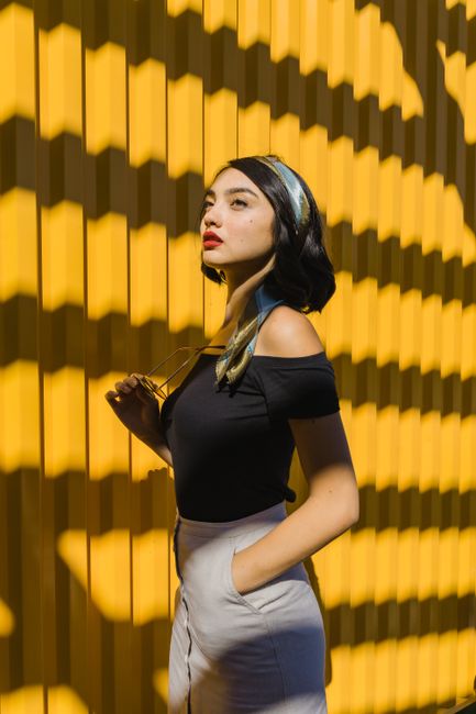Fashionable woman posing outdoors with striking shadows on a sunny day.