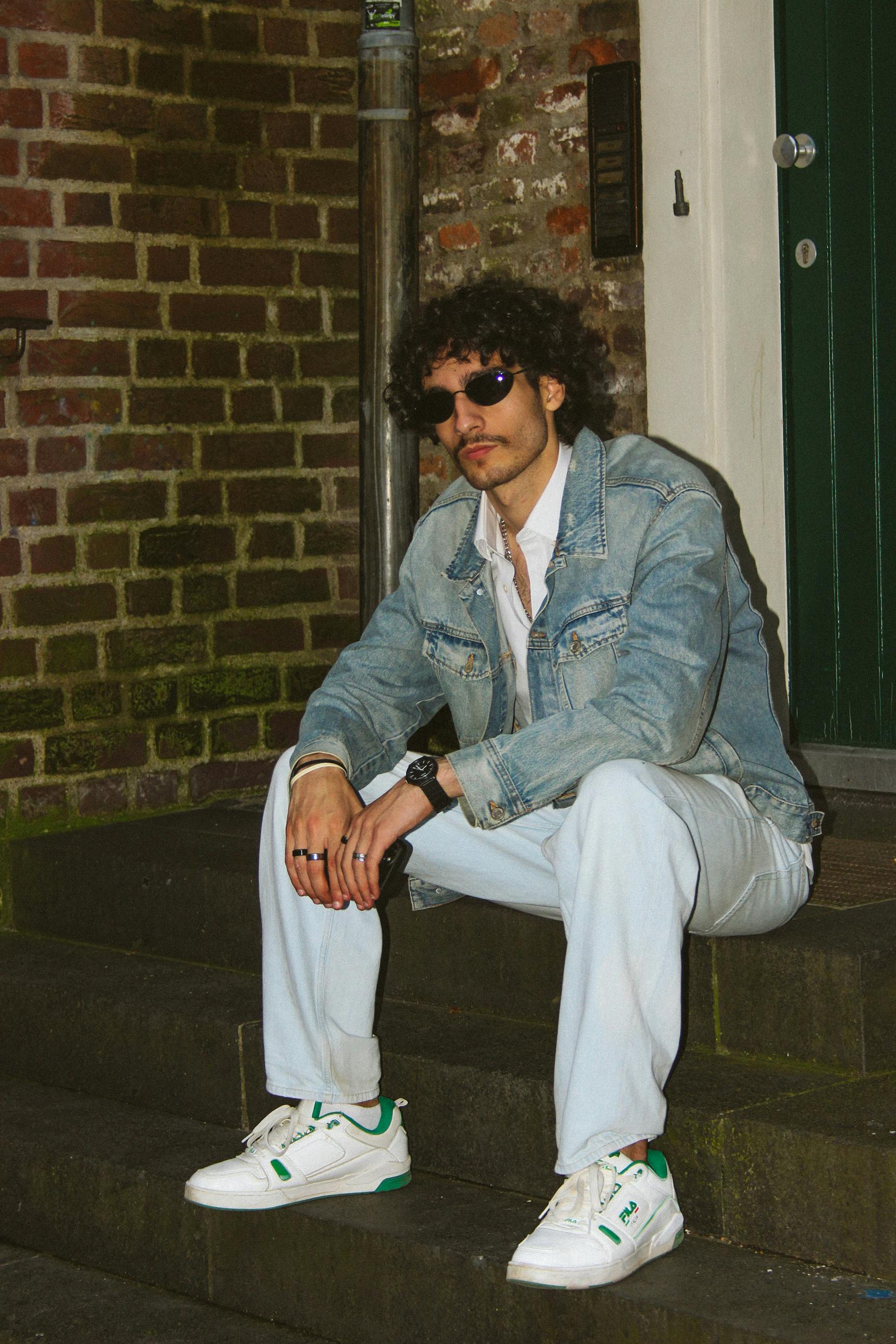 A fashionable man in denim and sunglasses sits on steps outdoors in Düsseldorf.