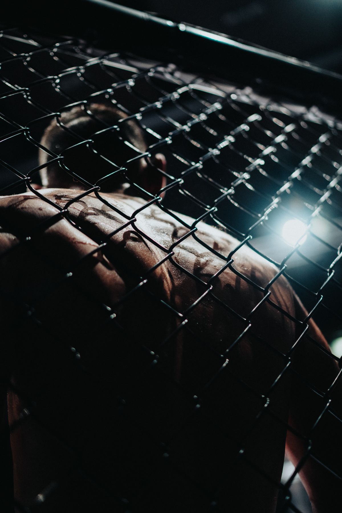 MMA fighter seen through a cage during intense training before a major fight night