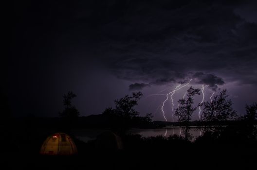 Capture of a vibrant lightning storm over a lake in Altai, Russia with tents in the foreground.