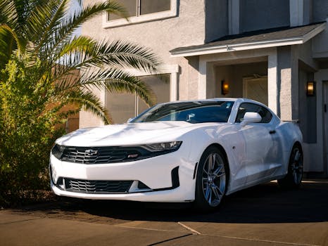 White sports car parked outside a modern house under palm trees.
