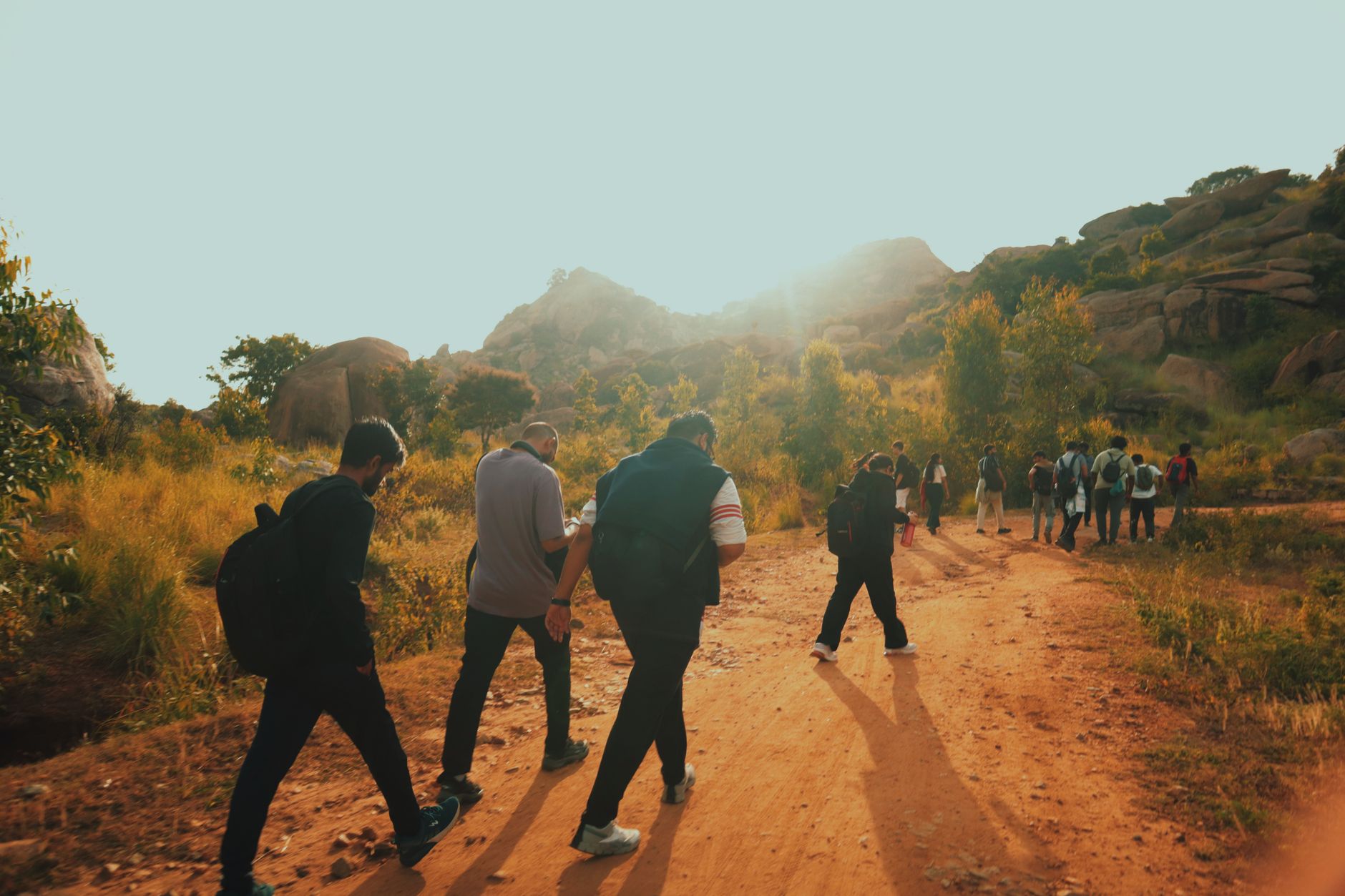 A group of adults hiking on a trail with scenic rocky terrain under clear skies.