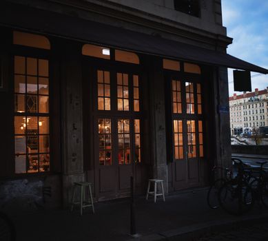 Warmly lit café exterior in a European city at twilight, creating a cozy ambiance.