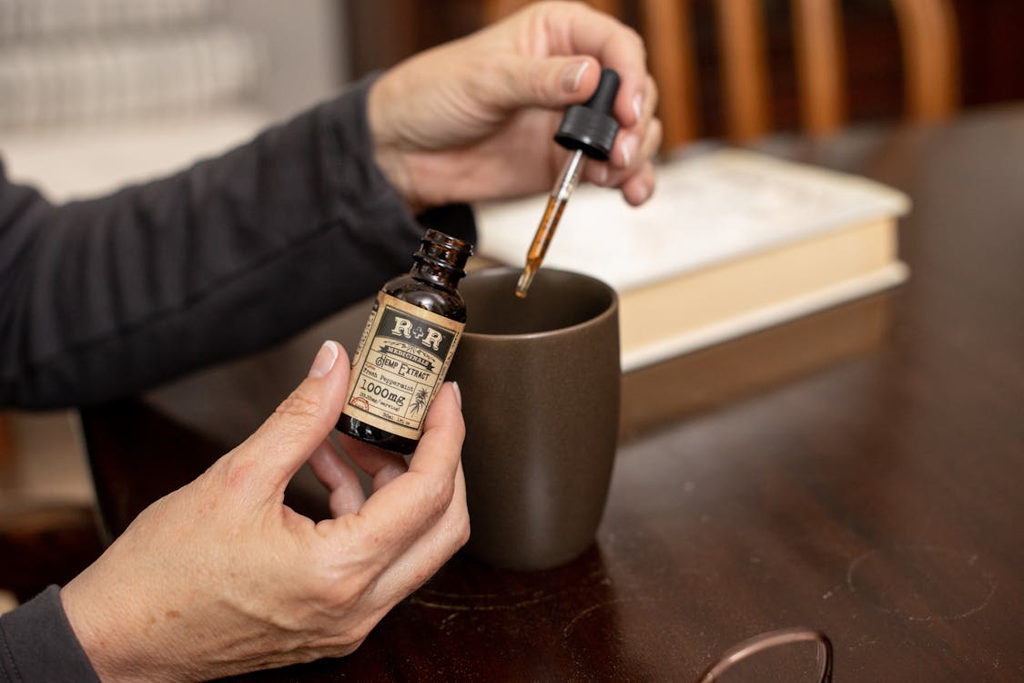 Free Close-up of hands using hemp extract oil with dropper into a cup indoors. Stock Photo
