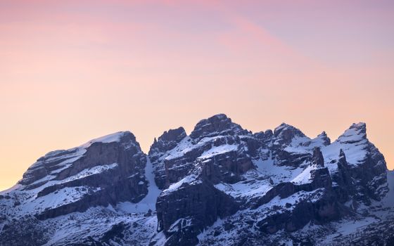 Breathtaking view of snowy mountain peaks against a pink sunrise sky, capturing nature's tranquil beauty.