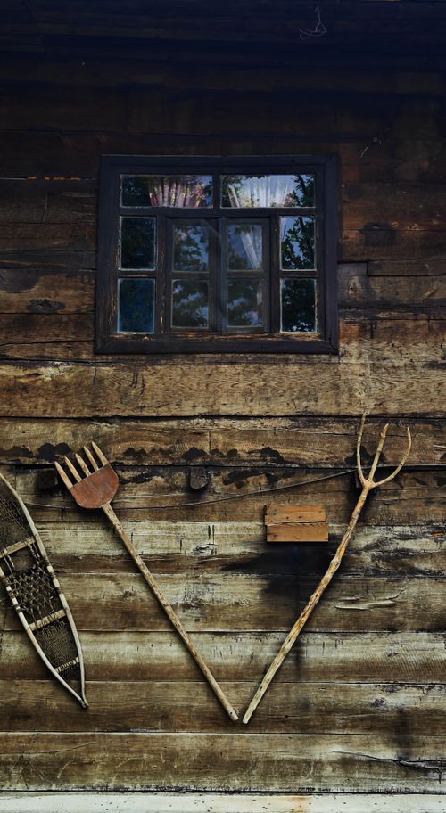 Free A quaint wooden wall features vintage tools and a window reflecting trees, evoking a rustic charm. Stock Photo