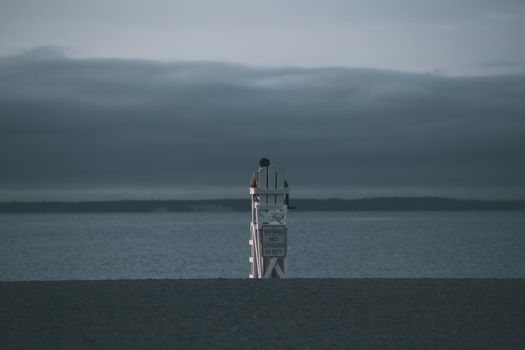 A lone lifeguard chair facing the calm early morning ocean under a cloudy sky, Stamford, CT.
