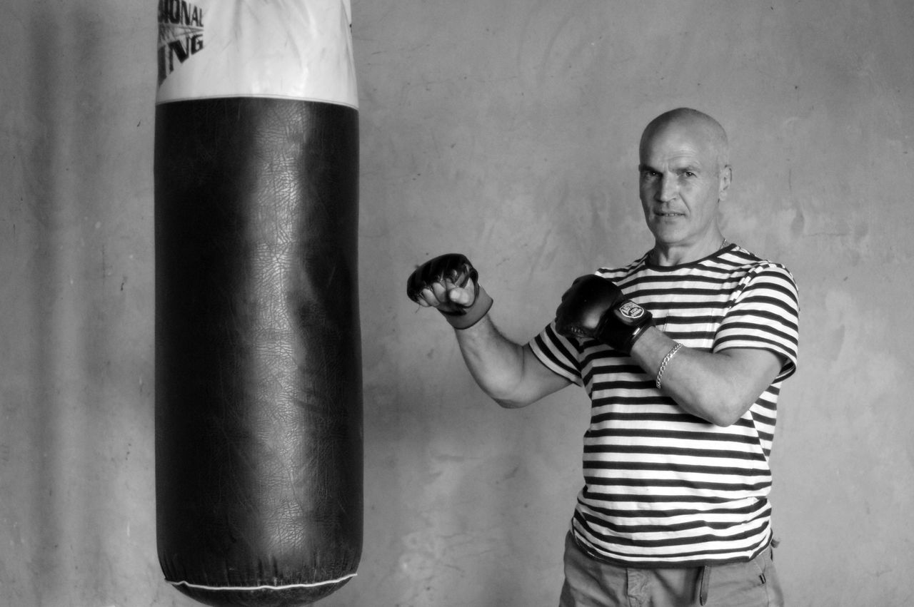 senior man in gloves practicing boxing with a punching bag indoors