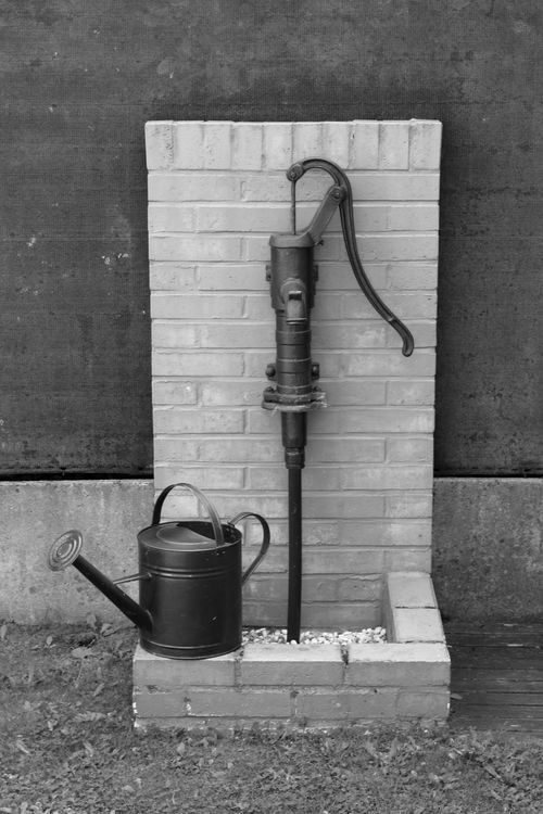 Free Classic black and white image of a vintage water pump with a metal watering can. Stock Photo