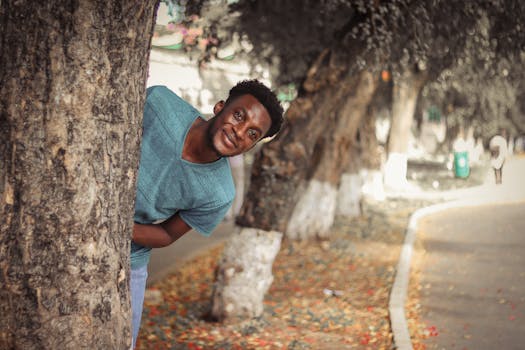 一个快乐的男子穿着休闲装，在公园的一棵树后面开玩笑地偷看