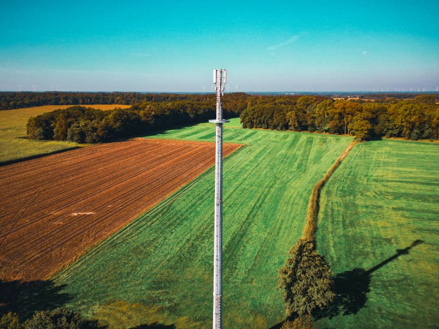 Aerial view of a telecom tower in a vibrant green field surrounded by forests.
