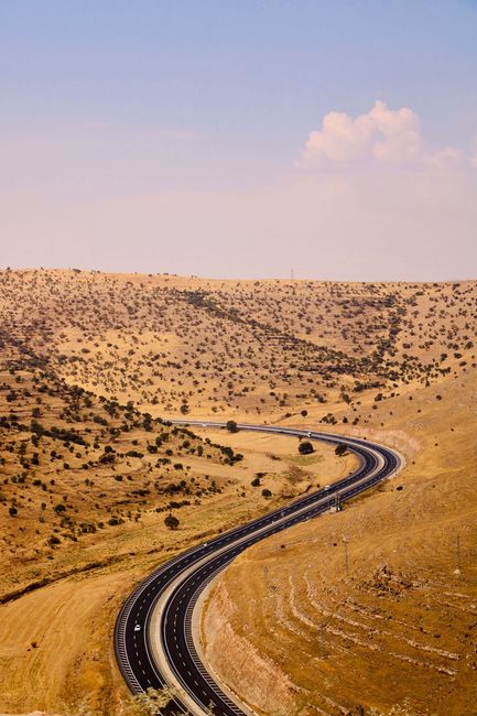 A picturesque winding road through the arid hills of Mardin, Türkiye under a blue sky.