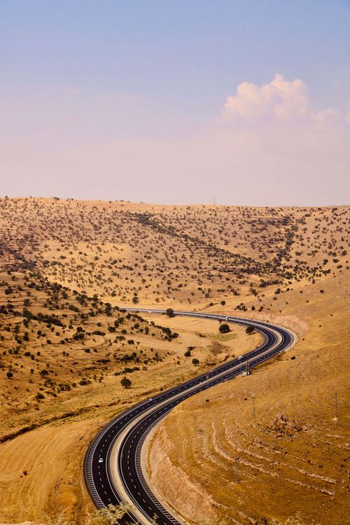 Free A picturesque winding road through the arid hills of Mardin, Türkiye under a blue sky. Stock Photo