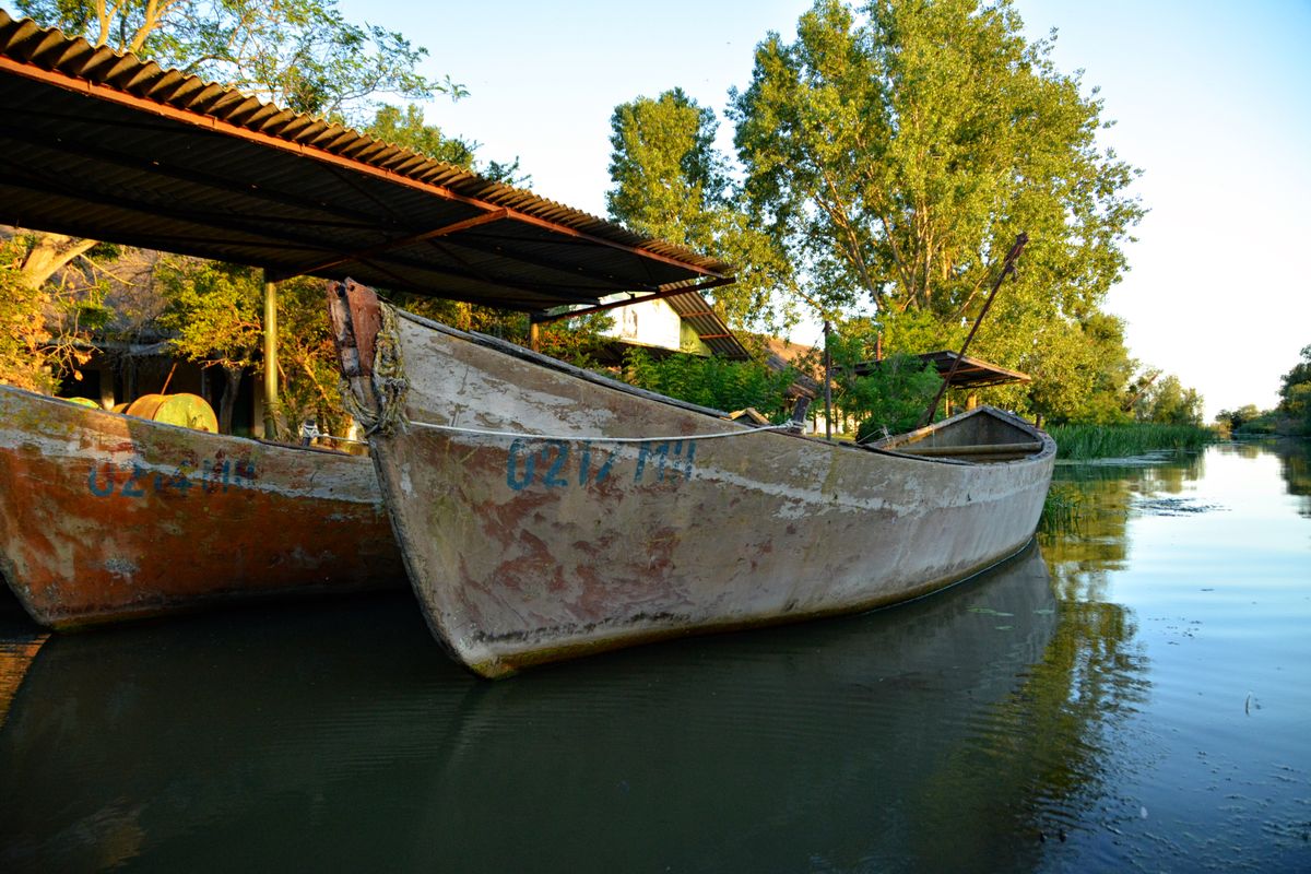 Doua lotci de lemn sub un sopron de tabla, pe canal, la apus