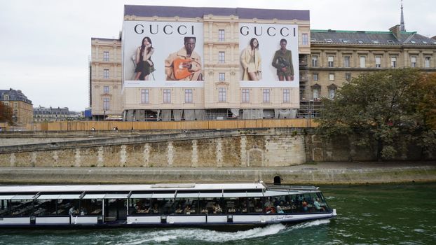 A Gucci advertising billboard by the Seine River in Paris with a passing cruise boat.