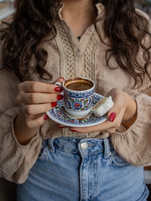 Close-up of a woman holding Turkish coffee and Turkish delight in a traditional setting.