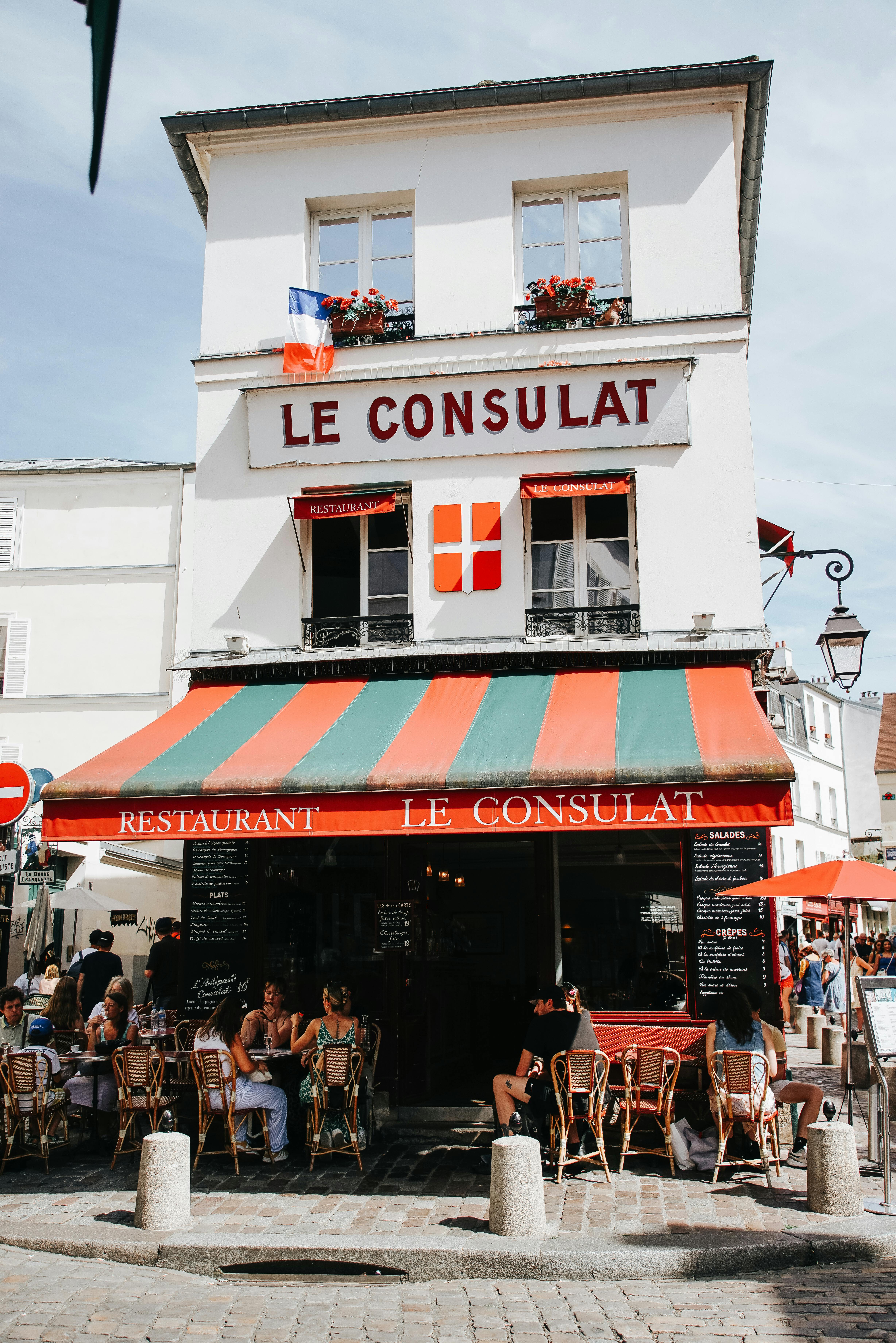 Quaint Parisian cafe 'Le Consulat' with outdoor seating in a sunny setting.