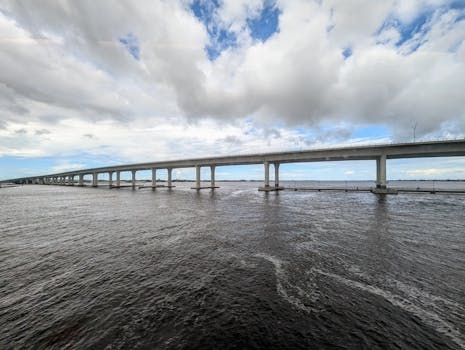 Wide view of a long bridge stretching across a vast river under an overcast sky.